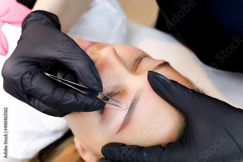 the permanent makeup master performs plucking of unnecessary hairs in the eyebrow area after the permanent makeup procedure