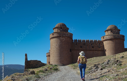 Woman with hat and small backpack going up a hill towards the medieval castle of La Calahorra (Granada, Spain) on a sunny spring day photo