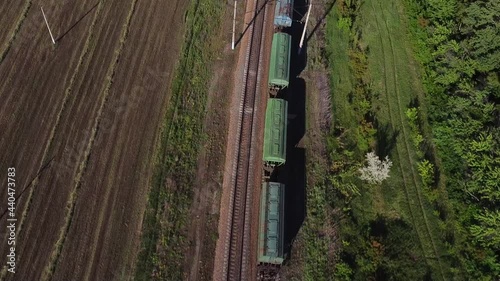 Railway transport. The locomotive pulls many different cars. Transportation of various goods. Green fields background. The video was taken from a drone.