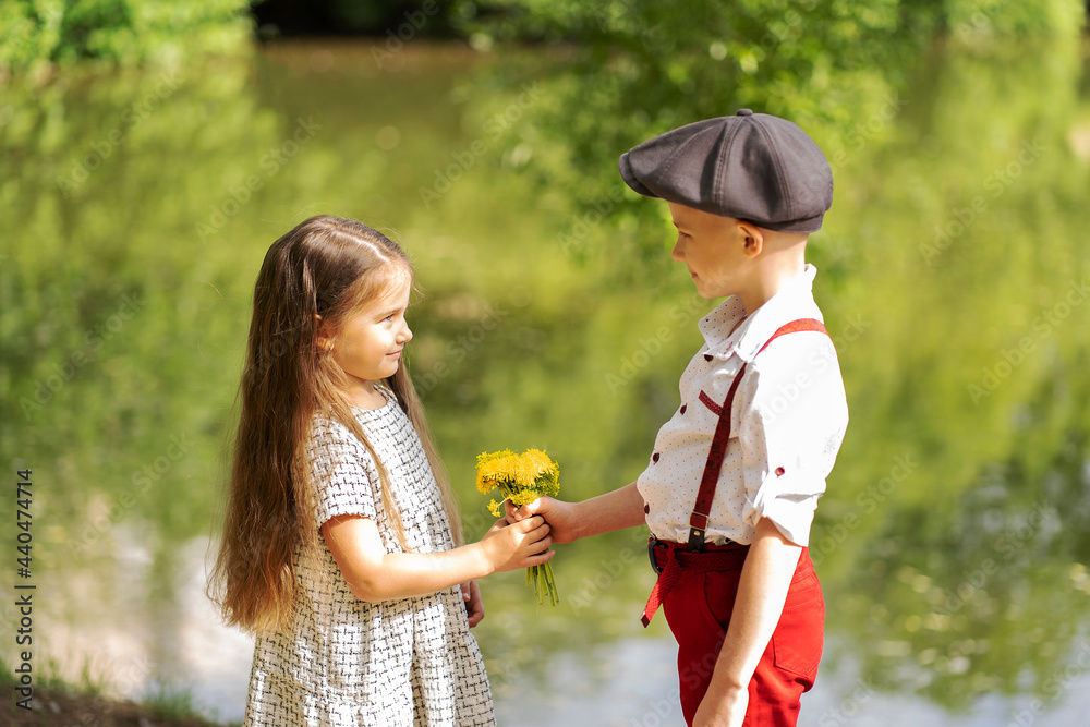 Fototapeta premium A little boy gives a girl a bouquet of wildflowers. Children stand in the park by the pond.