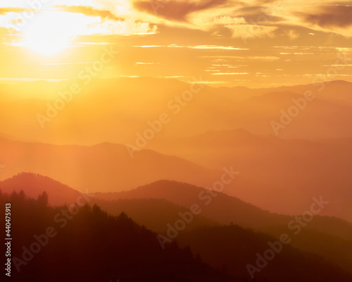 Sunset in the Smoky Mountains. The image is overly orange with a burst of sunshine in the upper left corner © Douglas