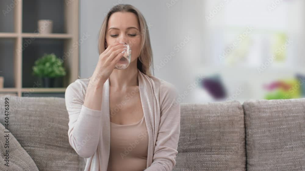 Portrait of beautiful young woman drinking refreshing pure water holding transparent glass at home Portrait of beautiful young woman drinking refreshing pure water holding transparent glass at home