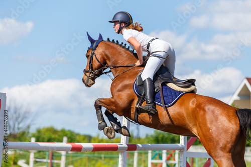 Fototapeta Young horse rider girl jumping over a barrier on show jumping course in equestri
