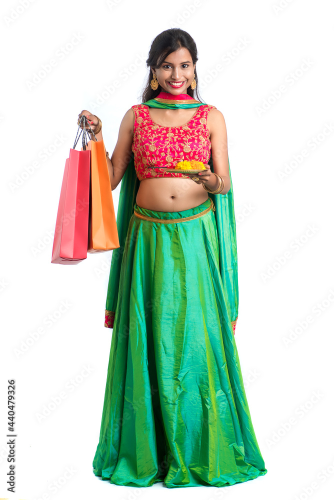 Beautiful Indian young girl holding and posing with shopping bags and pooja thali on a white background