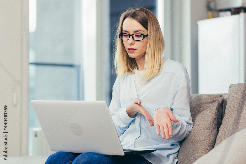 Beautiful blonde woman in casual clothes sitting on a sofa at home, and uses a laptop for video communication with friends and family Beautiful blonde woman in casual clothes sitting on a sofa at home, and uses a laptop for video communication with friends and family