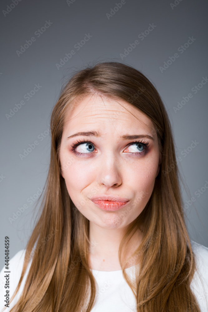 A beautiful girl sadly and with annoyance looks to the side pouting her lips. Isolated on gray background