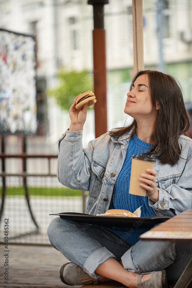 Obraz premium Street portrait of cheerful young woman eating fast food.