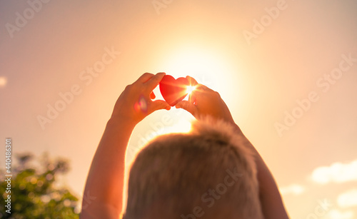 Child holding up heart to the sunset sky
