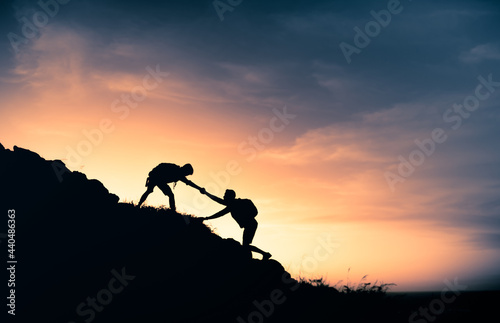 Hikers climbing a mountain giving a helping hand up the cliff. Teamwork, and never giving up concept.Team work, life goals and self improvement concept. 