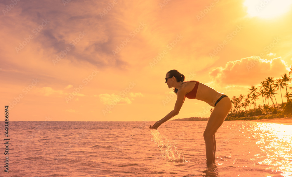 Happy young woman on a tropical beach at sunset playing splashing  in the water. Travel, vacation concept. 