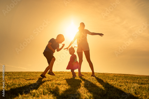 Mom and children dancing playing in a grass field. Family happiness concept. 