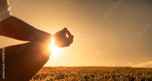 Close-up hand of a woman meditating on a grass field facing the sunset sky. Mind health, and wellness concept. 