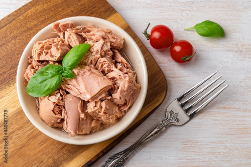 Top view of canned tuna in a bowl, fork and red cherry tomatoes on a white wooden table. Healthy eating snack of preserved tuna meat and fresh vegetables. Low calories tasty seafood. photo