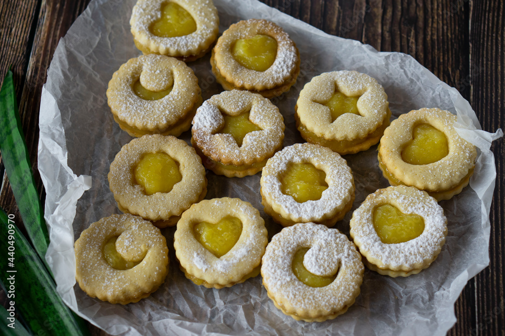 Linzer cookies with hearts, stars and moons with mango yellow curd (sauce) and powdered sugar on a old wooden background. Traditional dessert. Horizontal orientation.
