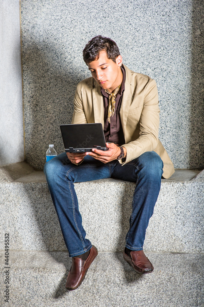 A young handsome businessman is sitting outside and working on a small computer.