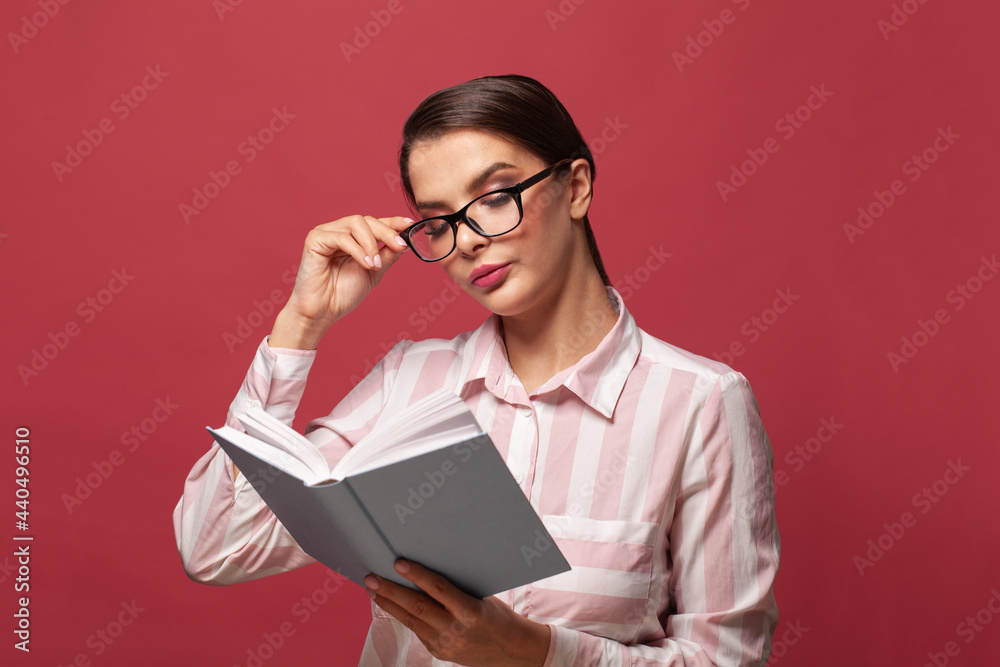 Pretty woman in white and pink shirt reading a book with empty blue cover on red background Pretty woman in white and pink shirt reading a book with empty blue cover on red background