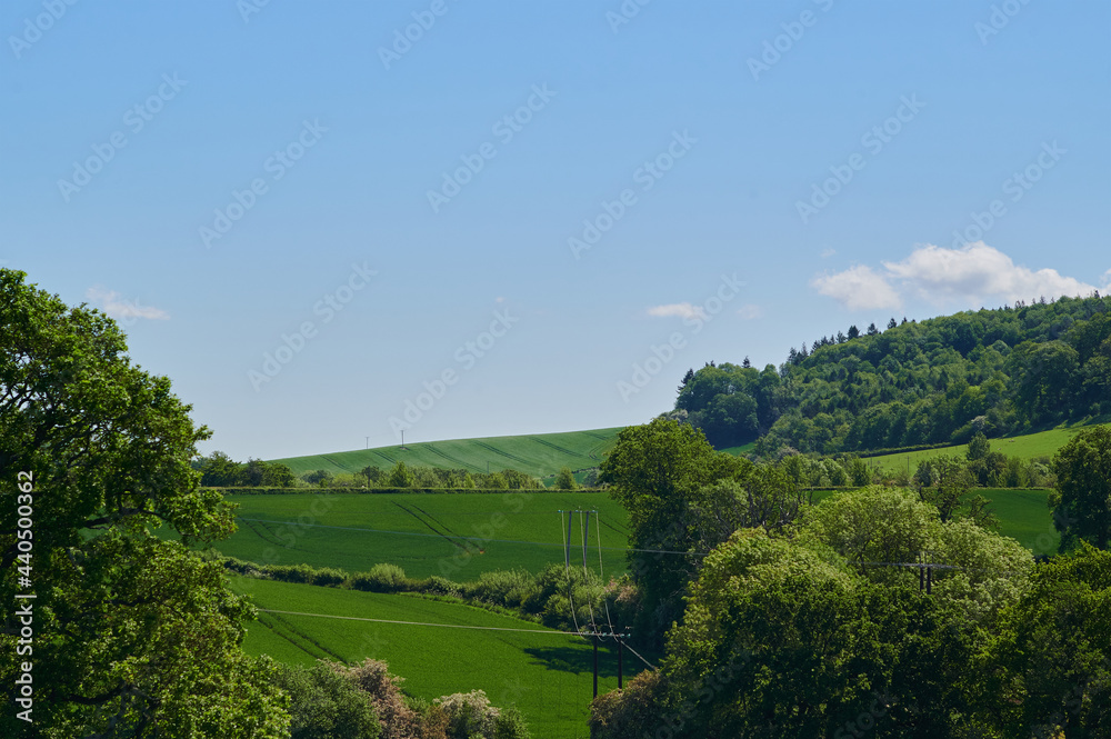 Agriculture farm field in english countryside with blue sky and low small clouds with hill in the background.