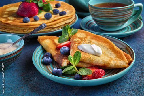 Pancakes with berries and sour cream on dark green background.  Maslenitsa. Shrovetide. Shrove Tuesday. Pancake Day. photo