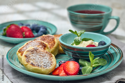 Russian cottage cheese pancakes (Syrniki) with berries and sour cream on light wooden background. Healthy breakfast