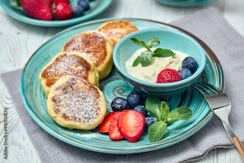 Russian cottage cheese pancakes  Syrniki  with berries and sour cream on light wooden background. Healthy breakfast