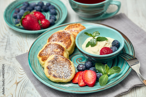 Russian cottage cheese pancakes (Syrniki) with berries and sour cream on light wooden background. Healthy breakfast