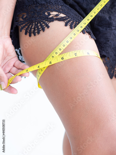 Authentic skin tan and slim fit woman measuring her leg with black pants. lose weight diet for shapely and good health care concept.