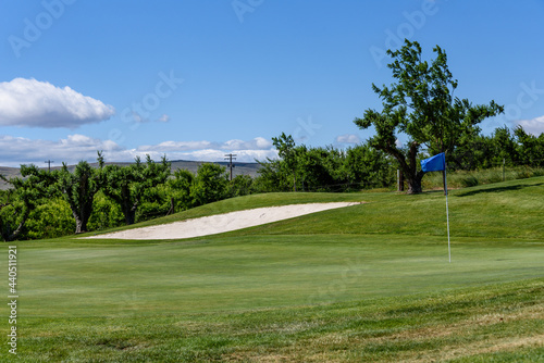 Sunny golf, sand bunker and fairway up to a green with scenic woodland and blue sky in the background 
