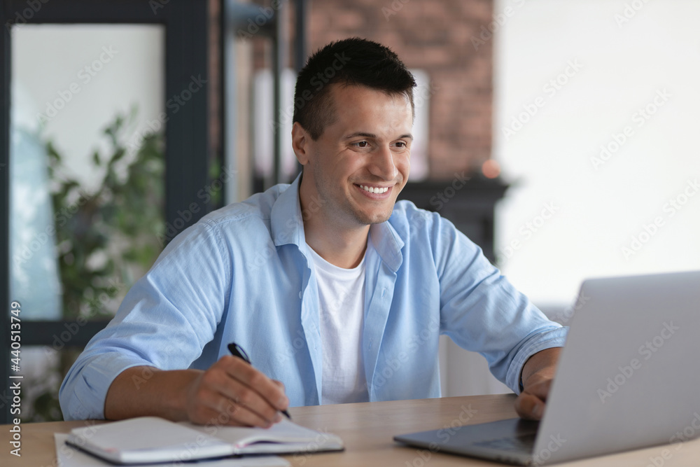 Friendly satisfied caucasian man student, taking notes in notebook during lecture sitting at table in home, online studying at home concept distance education, video call, smiling Friendly satisfied caucasian man student, taking notes in notebook during lecture sitting at table in home, online studying at home concept distance education, video call, smiling