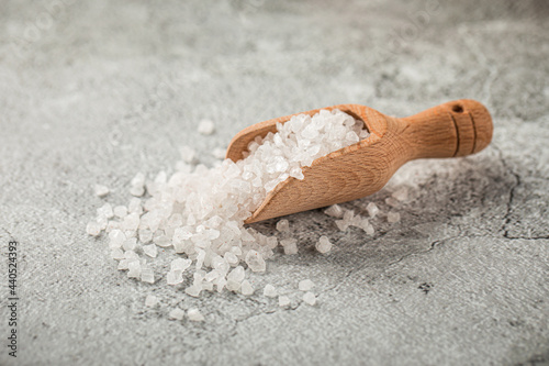 Heap of white salt in a wooden scoop on grey background