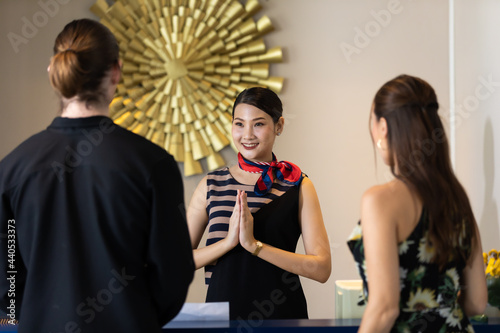beautiful young asian woman receptionists working at a reception desk make pay respect (sawasdee) to customer. photo
