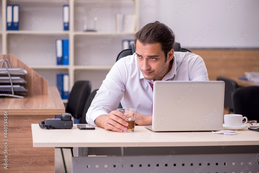 Young male employee drinking alcohol in the office Young male employee drinking alcohol in the office