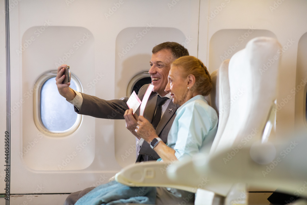 Happy Senior business man and mother passenger make selfie photo sitting in comfortable business class seat. Family travel together