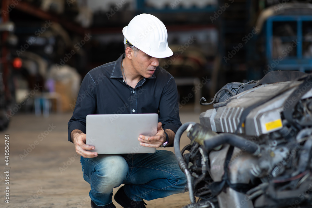 Mechanical man owner small business inspecting old car parts stock on laptop computer while working in old automobile parts large warehouse
