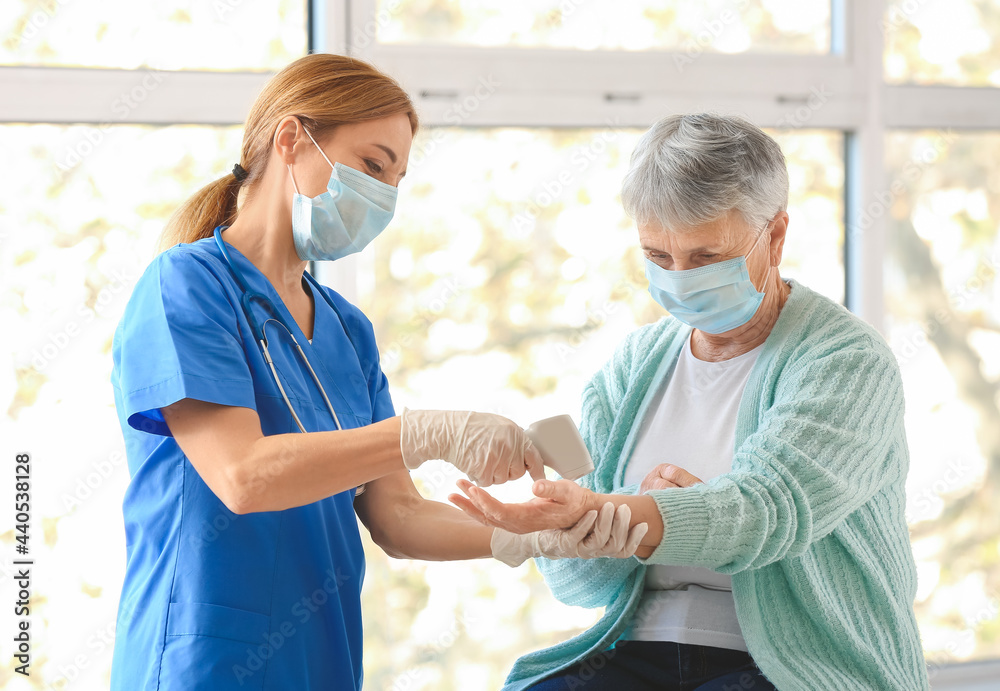 Doctor measuring temperature of senior woman in clinic
