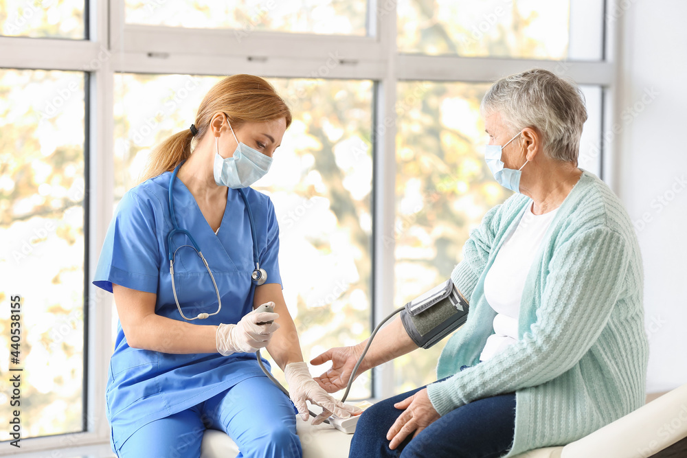 Obraz premium Doctor measuring blood pressure of senior woman in clinic