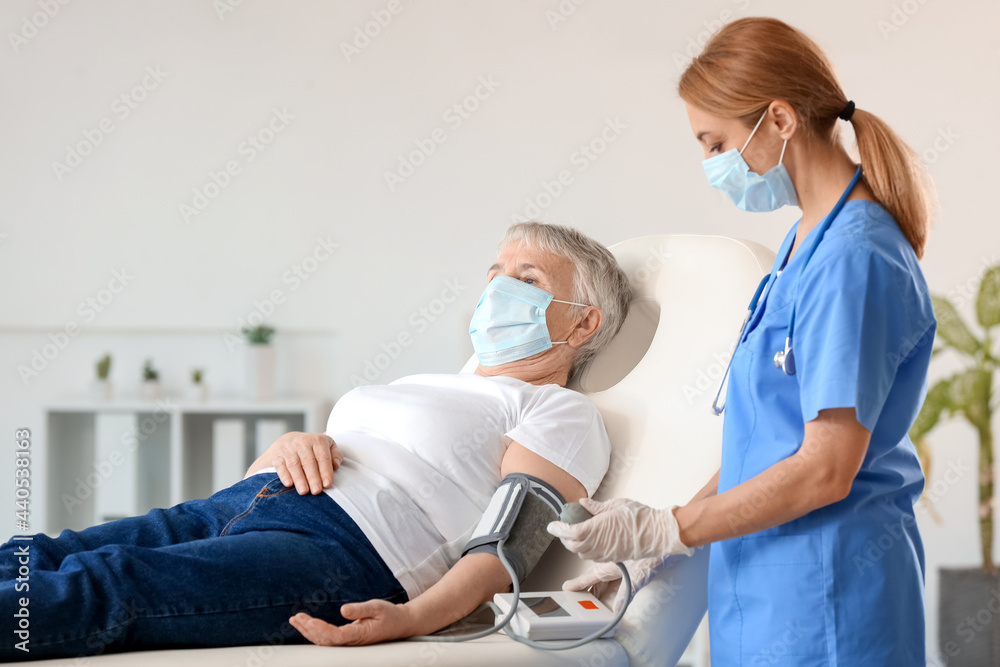 Obraz premium Doctor measuring blood pressure of senior woman in clinic