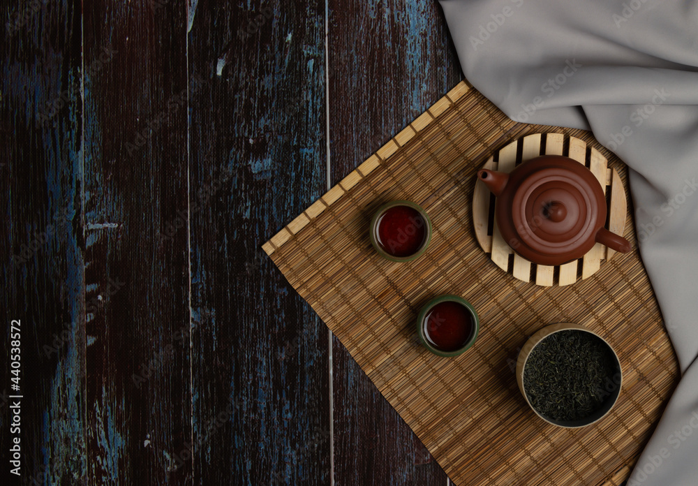 Chinese Tea Ceremony. Brown ceramic teapot and turquoise teacup. Green tea on a bamboo mat on an aged wooden table. Top view. Copy space Chinese Tea Ceremony. Brown ceramic teapot and turquoise teacup. Green tea on a bamboo mat on an aged wooden table. Top view. Copy space