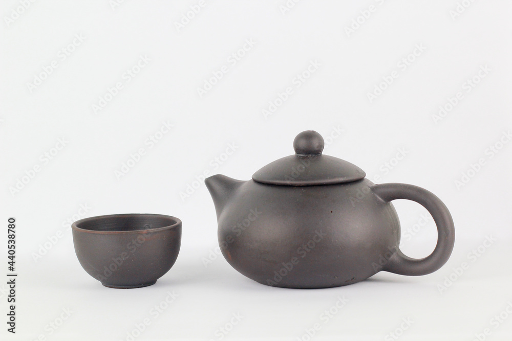 A Chinese black ceramic teapot and teacup isolated on a white background.