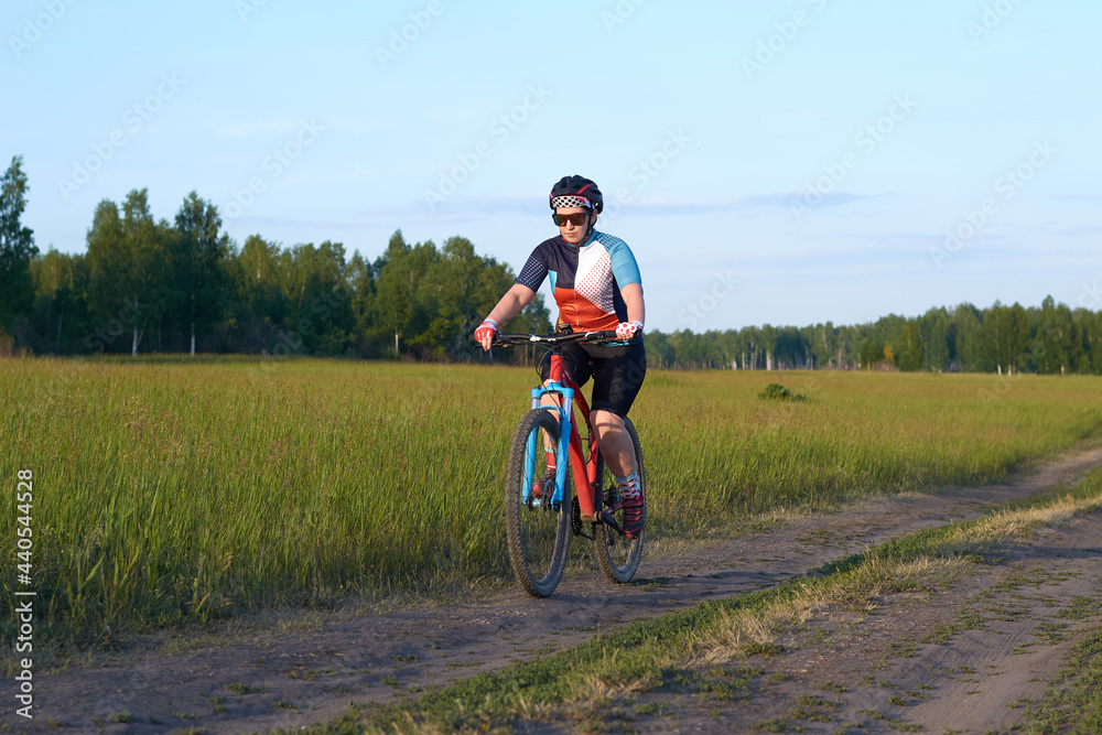 The girl rides a mountain bike on a field road. Endurance training, tempo or interval. Healthy lifestyle. Weight loss by sports. Hobby of a modern person.