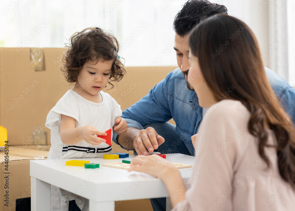 Parents and daughters play with wooden blocks sitting on the floor in the living room at home. The family just moved to a new house. Happy moment Multi-ethnic dad mom and child. Parents and daughters play with wooden blocks sitting on the floor in the living room at home. The family just moved to a new house. Happy moment Multi-ethnic dad mom and child.
