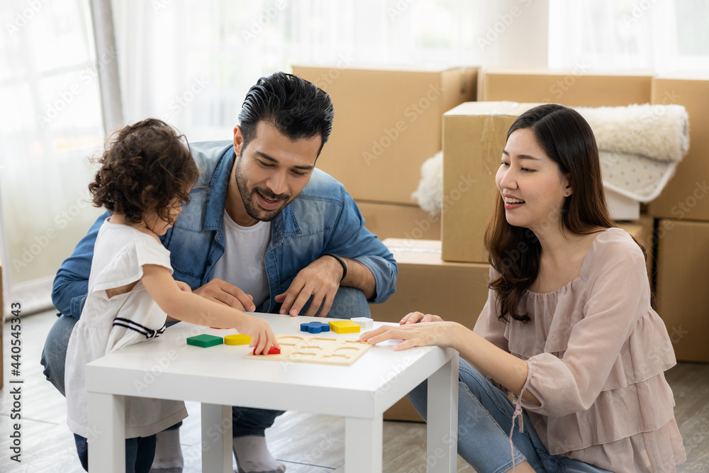 Parents and daughters play with wooden blocks sitting on the floor in the living room at home. The family just moved to a new house. Happy moment Multi-ethnic dad mom and child.