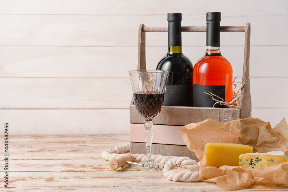 Naklejka premium Box with bottles of wine, cheese and glass on light wooden background