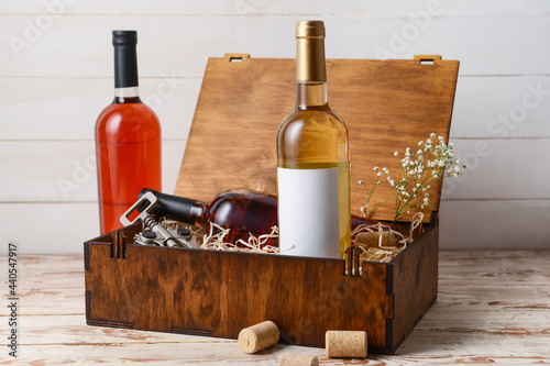 Box with bottles of wine and corkscrew on light wooden background photo
