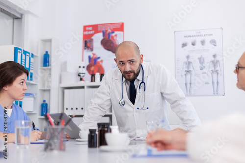 Radiologist doctor man explaining healthcare treatment to medical teamwork while standing at desk in conference meeting room. Hospital team planning diagnosis expertise presenting science examination