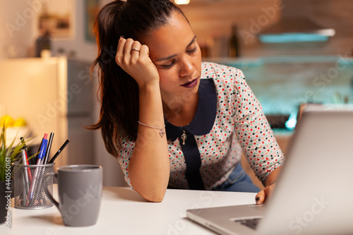 Woman resting eyes while working from home kitchen during a deadline late at night. Employee using modern technology at midnight doing overtime for job, business, career, network, lifestyle ,wireless. photo