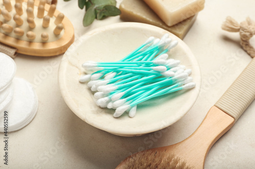 Plate with cotton swabs, comb, brush and buds on light background, closeup
