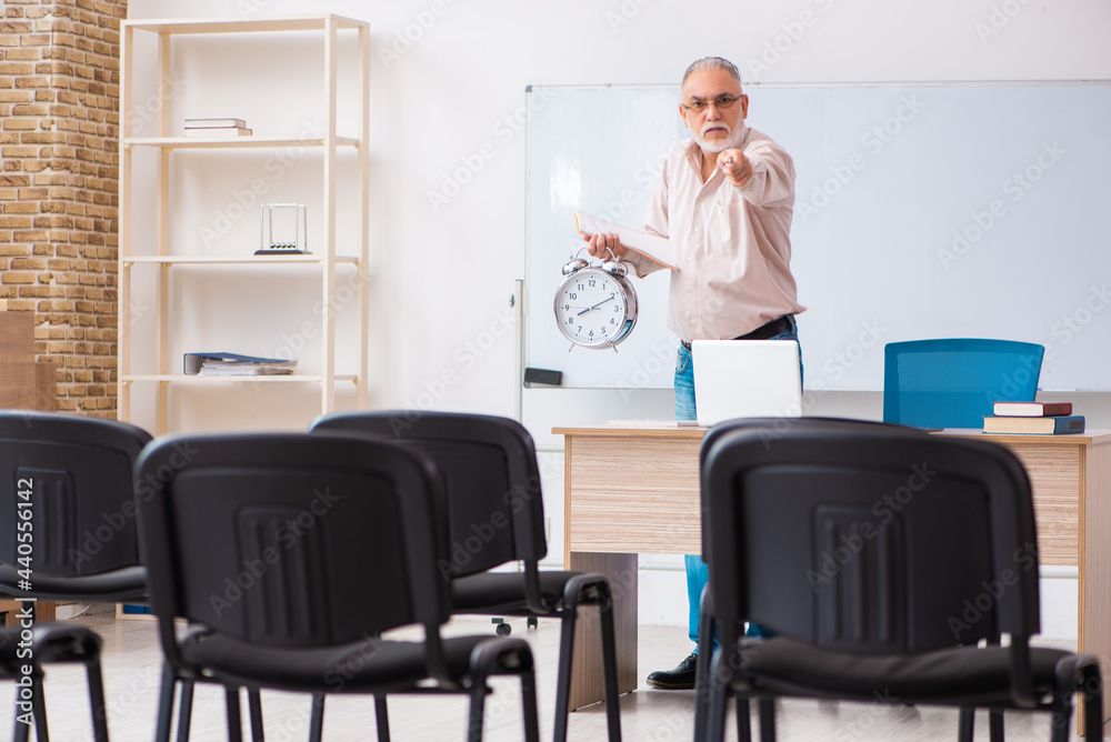 Old male teacher in the classroom in time management concept