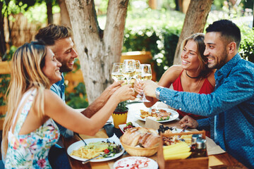 Group of young happy people toast with wine at lunch in restaurant during a sunny summer day