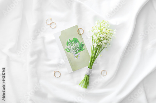 Beautiful lily-of-the-valley flowers, rings and greeting card on light fabric background
