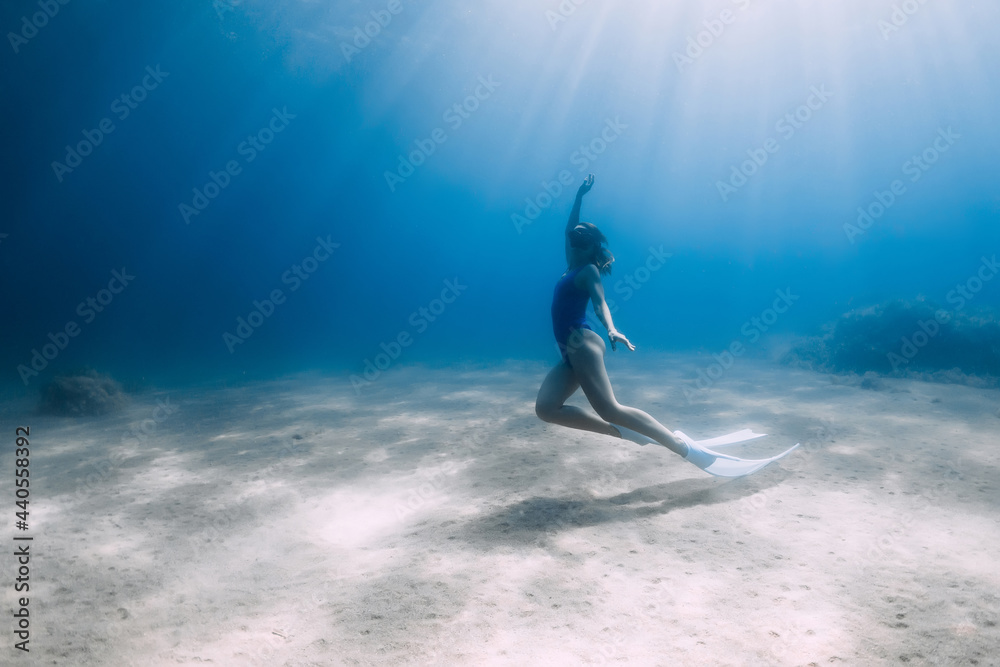Lady freediver posing underwater at the deep in blue sea with sunlight.